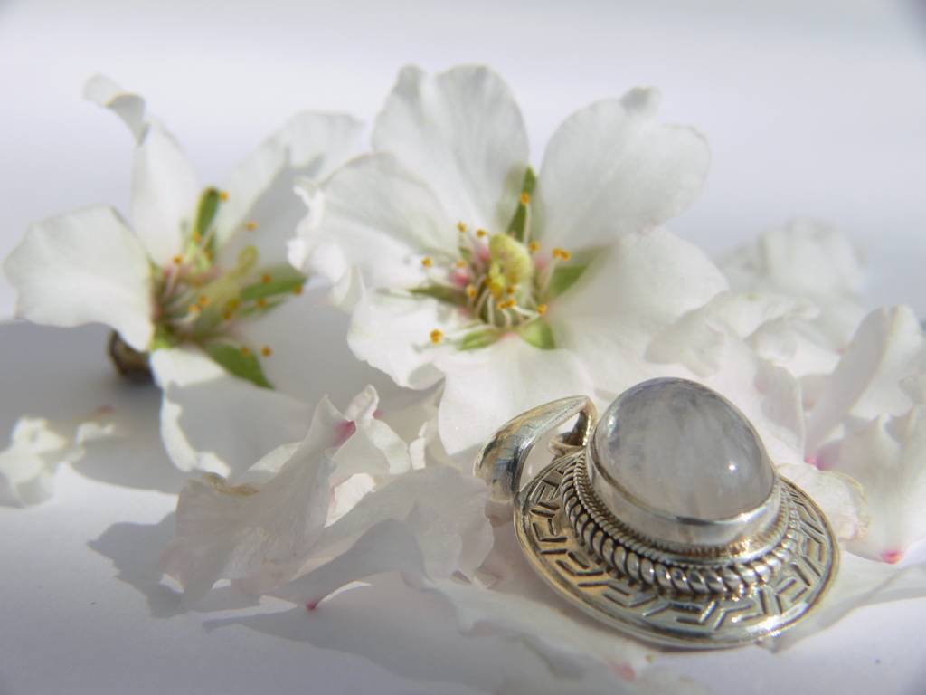 Un pendentif serti d'une pierre de lune posé près de fleurs blanches